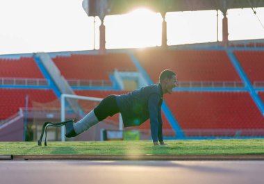 Bacağında protezi olan sporcu bir sporcunun yan görünüşü yere yatar ve şınav hareketi de stadyumdaki antrenmandan önce ısınmayı dört gözle bekler..