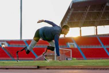 Sporcu atlet protez bacakları koşmaya başlama pozisyonunda kalsın ve akşamın yumuşak ışıklarıyla stadyuma baksın..