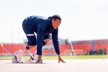 Stadyumdaki pistte koşmaya başlamak için bacak hareketi üzerine protezi olan sporcu bir sporcunun yan görüntüsü. Spor konsepti.