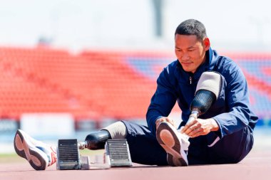Bacağında protez olan sporcu bir sporcu stadyumdaki ayakkabı bağcıklarını bağlamak için koşu ekipmanının yanına oturur. Spor konsepti.