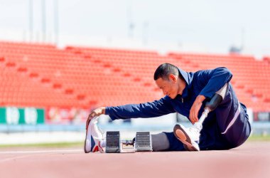 Bacağında protezi olan sporcu bir sporcu. Stadyumdaki koşu ekipmanlarının yanında oturup geriniyor. Spor konsepti.
