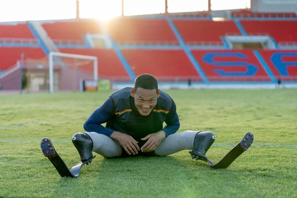 Sport man athlete prosthesis legs sit down on grass field and separate his legs also bend down the head in the stadium.