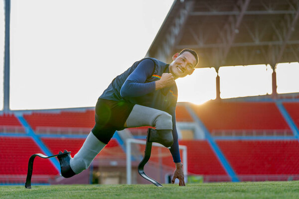 Close up side view sport man athlete prosthesis legs stay in the position of stretching also look at camera in the stadium with soft light of evening.