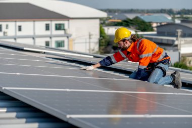 Sanayi teknisyeni fabrika binasının çatısındaki güneş pillerini kontrol etmek ve onarmak için dokunuyor. Yeşil ve sürdürülebilir enerji kavramı iyi çevreye.
