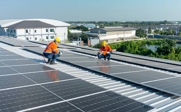 两名高加索技术人员坐在屋顶上 讨论如何维护工厂或大楼屋顶上的太阳能电池板 绿色和可持续能源概念 免版税图库图片