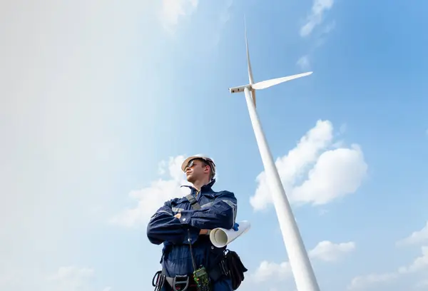 Professional technician worker man stand with arm-crossed also look to left side and stand in front of wind turbine or windmill with blue sky in concept of green energy for good environment.