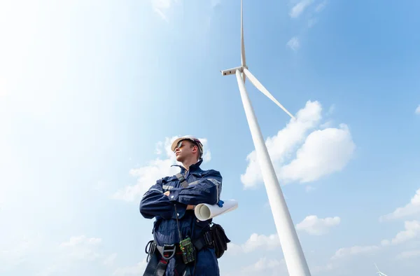 Professional technician worker man stand with arm-crossed and stand in front of wind turbine or windmill with blue sky in concept of green energy for good environment.