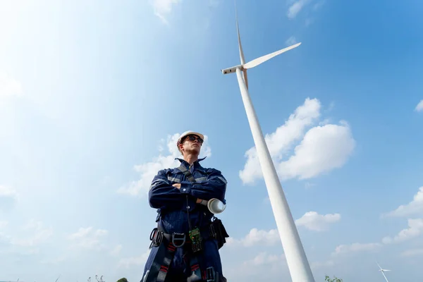 Professional technician worker man stand with arm-crossed and stand with look to right side in front of wind turbine or windmill with blue sky in concept of green energy for good environment.