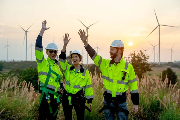 参考译文 在发电厂附近的风车或风力涡轮机制造厂前 一群技术工人手牵着手站着 表达工作时的快乐心情 图库照片