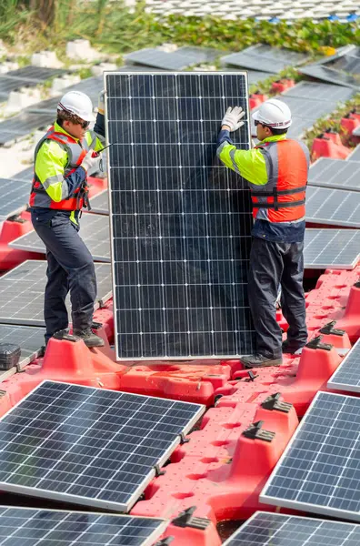 Vertical image of two professional technician workers stand and hold solar cell panel to check and maintenance the system in concept of green energy power plant for good environment.