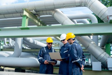 Mühendis ya da fabrika teknisyeni işçi ekibi petrokimyasal gaz boru hattının yanında durur ve işleri hakkında konuşmak için dizüstü bilgisayarı kullanır..