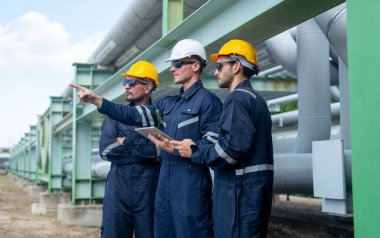 Mühendis ya da fabrika teknisyenlerinden oluşan bir grup petrokimyasal gaz boru hattının yanında duruyor ve çalışmalarını bir puan ileri alarak tartışmak için tablet kullanıyorlar..