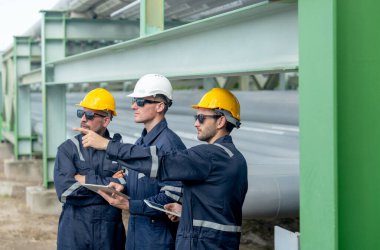 Mühendis ya da fabrika teknisyenlerinden oluşan yan görüş grubunu kapatın petrokimyasal gaz boru hattının yanında durun ve tableti kullanarak çalışmalarını bir puan ileri alarak tartışın..