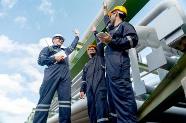 Mühendis ya da fabrika teknisyenlerinden oluşan bir grup petrokimyasal gaz boru hattının yanında duruyor ve çalışmalarının başarısından duyduğu mutluluğu ifade etmek için ellerini kaldırıyor..