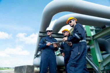 Mühendis veya fabrika teknisyeni ekibinin yan görünüşü, işyerindeki boru hattına da işaret eden petrokimyasal gaz boru hattının altında duruyor.