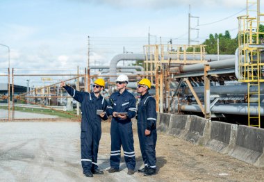Mühendis ya da fabrika teknisyenlerinden oluşan bir grup petrokimyasal gaz boru hattının yanında duruyor ve çalışmalarını tartışmak için tablet kullanıyorlar..