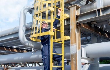 Fabrika mühendisi veya teknisyeni, çalışmak veya işyerinde bakım yapmak için petrokimyasal gaz boru hattının merdivenlerine tırmanıyor..