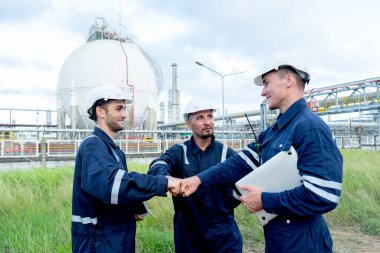 Bir grup mühendis ya da teknisyen, petrokimya fabrikasında tankın önünde duruyor ve ilk çarpışmada birbirlerine bakıyorlar..