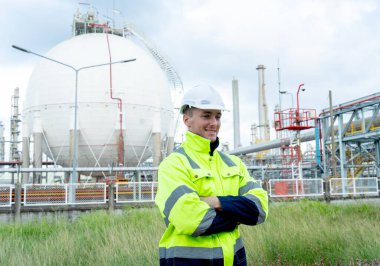 Mühendis ya da teknisyen portresi elinde telsizle ayakta duruyor ve kolları çaprazlanmış bir şekilde petrokimya tankının önünde duruyor..