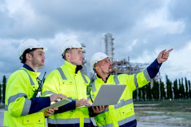 Bir dizüstü bilgisayarı olan fabrika mühendisi ya da teknisyeni ya da teknisyen işçiler tablet tutarken aynı zamanda akşam ışığı sırasında rafineri ve petrokimya fabrikasının önünde duruyor..