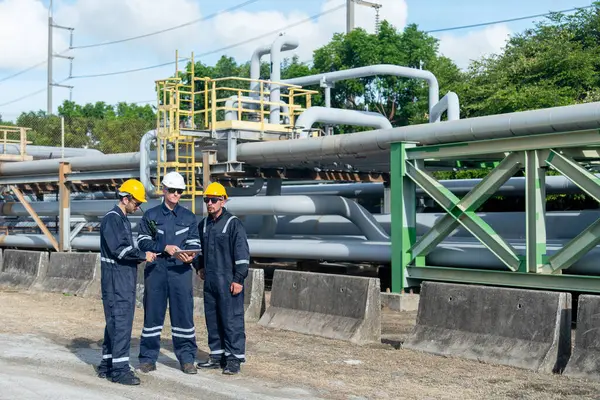 Mühendis ya da fabrika teknisyenlerinin geniş açılı görüntüleri petrokimyasal gaz boru hattının yanında duruyor ve iş yerlerindeki çalışmaları hakkında konuşmak için tablet kullanıyorlar..