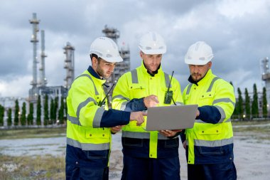 Bir grup mühendis ya da teknisyen, petrokimya fabrikasının önünde duruyor ve bilgisayarla işlerini tartışıyorlar..