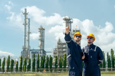 Bir tabletli iki fabrika mühendisi veya teknisyen, iş arkadaşına işi açıkla ve gün ışığında petrokimya fabrikasının önünde dur..