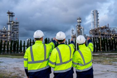 Mühendis ya da teknisyen işçiler kolları bağlı ve fabrikaya bir puan uzaklıktalar ve gökyüzü bulutlu fırındaki petrokimya fabrikasına bakıyorlar..