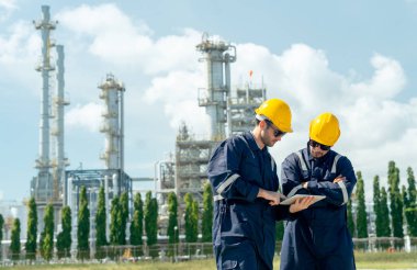 İki fabrika mühendisi veya teknisyeni tabletle tartışıyor ve gün ışığında rafine ve petrokimya fabrikasının önünde duruyorlar..