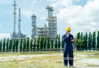 Fabrika mühendisi ya da teknisyen, iş arkadaşlarıyla konuşmak için telsiz bağlantısı kurar ve gün ışığında rafine ve petrokimya fabrikasının önünde durur..