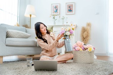 Güzel Asyalı bir kadının yan görünüşü yere oturup, evinde çiçeklerle mutlu mesut oturması..