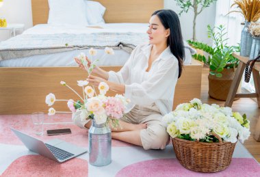 Güzel Asyalı kadın rahatça dinlenebilmek için evinin yatak odasında çiçek aranjmanı yapmaktan mutluluk duyar..