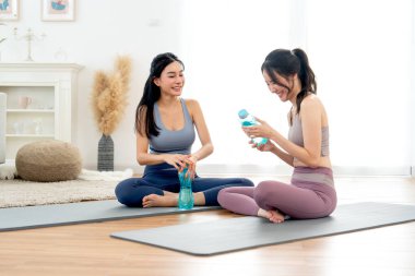 Egzersiz elbiseli iki Asyalı kadın yoga minderinde oturup sohbet etmekten ve evde antrenman yaptıktan sonra dinlenmekten zevk alırlar..