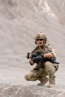 Silahlı bir asker ya da bir asker dağın yakınındaki savaş meydanında oturur ve dışarıda antrenman yaparken ileriye bakar..