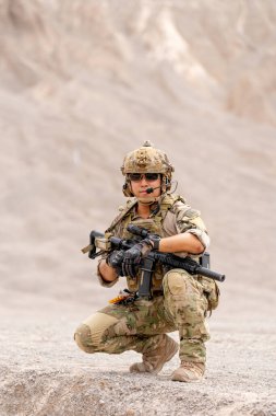 Silahlı asker ya da askerin dikey görüntüsü. Dağın yakınındaki savaş meydanında oturup açık hava tatbikatı sırasında kameraya bakın..
