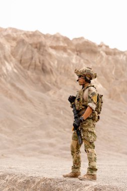 Silahlı asker ya da askerin dağın yakınındaki savaş alanında dikey görüntüsü. Açık hava antrenmanı sırasında sol tarafa bakın..