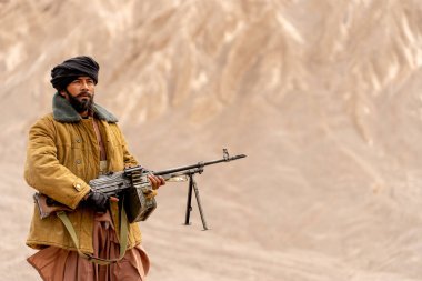 Kostümlü adam teröristlere benziyor. Silahı var ve dağın önünde dur ve önüne bak..