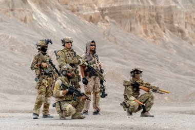 Farklı silah ya da silah türlerine sahip asker ya da askerlerden oluşan yan görüş ve portre grubu açık alan alanındaki kireçtaşı dağının önünde dururlar..