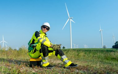 Rüzgar türbini işçisi ya da teknisyeni alet çantasına oturur ve cep telefonu kullanır. Çalışma sırasında kameraya da bakın..