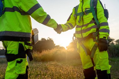 Rüzgâr türbini ya da yel değirmeni işçisi ya da teknisyenlerden ikisini kapatın ve arka planda gün batımından gelen sıcak ışıkla işyerinde durun..