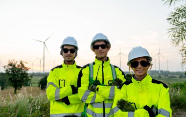 Rüzgâr türbini işçilerinin ya da teknisyenlerin portre grubu kolları çapraz durarak arka planda rüzgar türbini sırasına göre kameraya bakıyor..