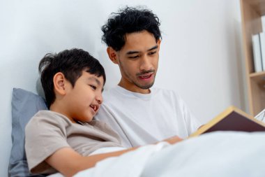 Yakından bak Asyalı genç baba oğlunun yanına otur ve mutlu bir şekilde kitabı oku..
