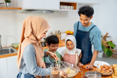 Muslim mother show example to mix flour in the bowl for her child to make the bakery in kitchen of their house. clipart