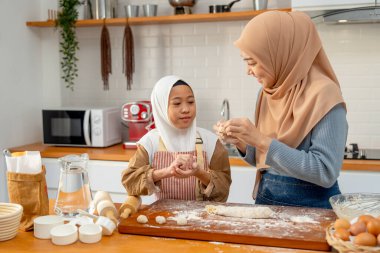 Asyalı Müslüman bir anne kızına evinin mutfağında birlikte fırın yapmak için top şeklinde un harmanlamayı öğretiyor..