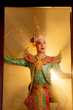 Khon maskeli bir adamın dikey görüntüsü İlah olarak ayakta duruyor ve arka planda ışık huzmesi olan eski binanın kapısının önünde performans eylemi var..