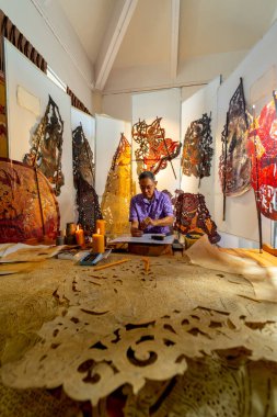 Dikey görüntü Asyalı kıdemli adam çekiç ve keski kullanarak büyük gölgeler yaratıyor ve işyerinin etrafında çeşitli ürünler bulunan işyerinde çalışmaya konsantre oluyor..