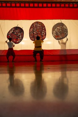 Vertical image of three player men stand with perform grand shadow play with two stay in front of white screen with reflection on the floor. clipart