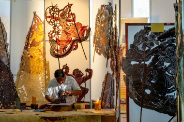 Asyalı kıdemli bir adam büyük gölge oyun sanatı yaratmak için çekiç ve keski kullanır ve işyeri çevresinde çeşitli ürünlerle birlikte iş yerinde çalışmaya konsantre olur..