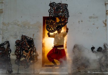 Bir adam Grand Shodow 'un sanatını kapının önünde oynatıyor. Çerçevenin önünde de eski binanın önünde el sanatları ve odanın arkasında sıcak bir ışık var..