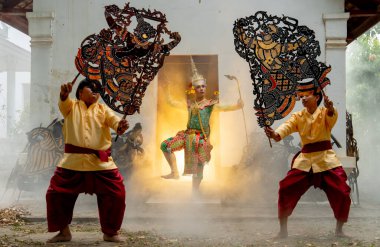 Khon maskeli bir adam melek olarak ayağa kalk ve eski binanın kapısının önünde gösteri yap. Ayrıca iki adam ön tarafta büyük bir gölge, arka tarafta ise sıcak bir ışık tut..